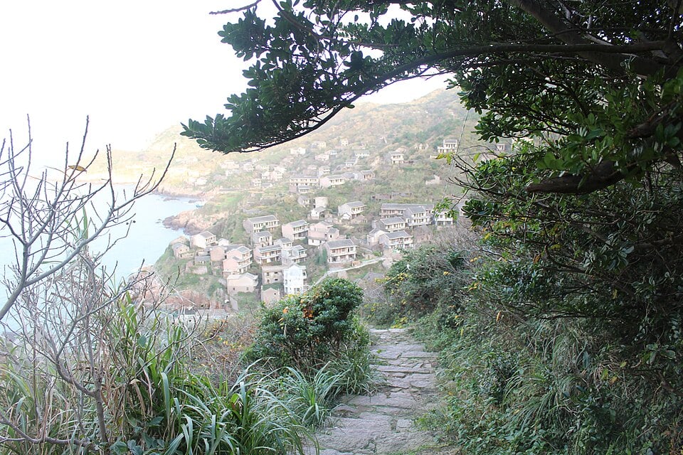 A hillside view of Houtouwan, with former village buildings and vegetation.